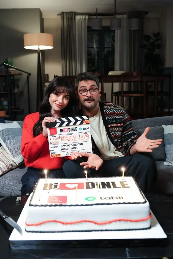 Başrol oyuncuları kanepede dizi klaketi ve pastayla poz veriyor.