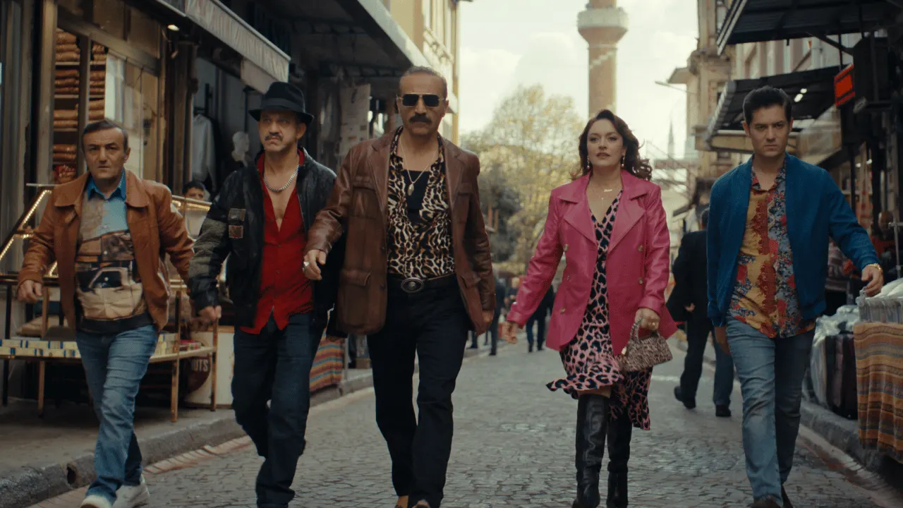 Asım Noyan ve ekibi dar bir sokakta birlikte yürüyor.