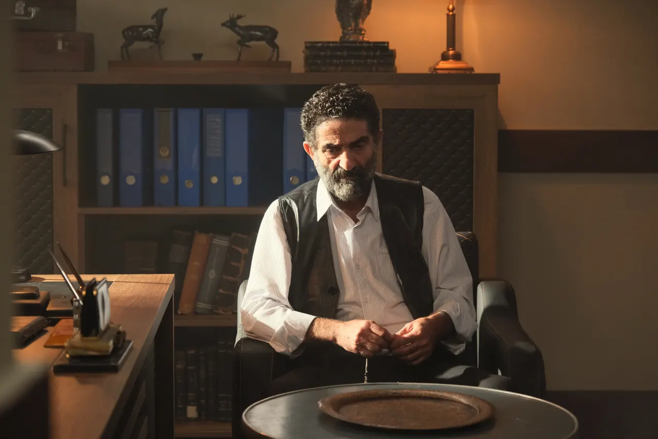 Sakallı erkek çalışma masasının arkasında oturuyor.